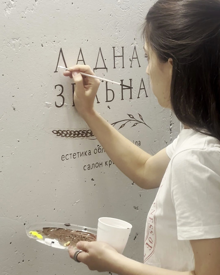Художниця вручну розписує знак «Ладна-Звабна» на стіні нового салону